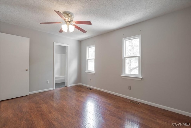 unfurnished bedroom featuring multiple windows, wood finished floors, a textured ceiling, baseboards, and ensuite bath