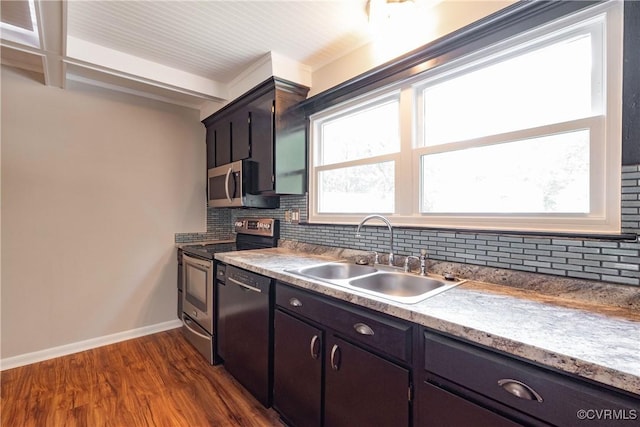 kitchen featuring a sink, appliances with stainless steel finishes, backsplash, dark wood-type flooring, and baseboards