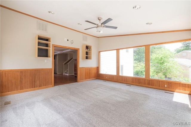 carpeted empty room featuring wainscoting, wooden walls, a ceiling fan, ornamental molding, and recessed lighting