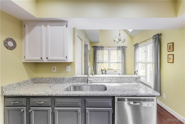 kitchen featuring dishwasher, a sink, a chandelier, dark wood-style flooring, and a peninsula