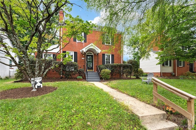 view of front of house with brick siding, a front lawn, and a chimney
