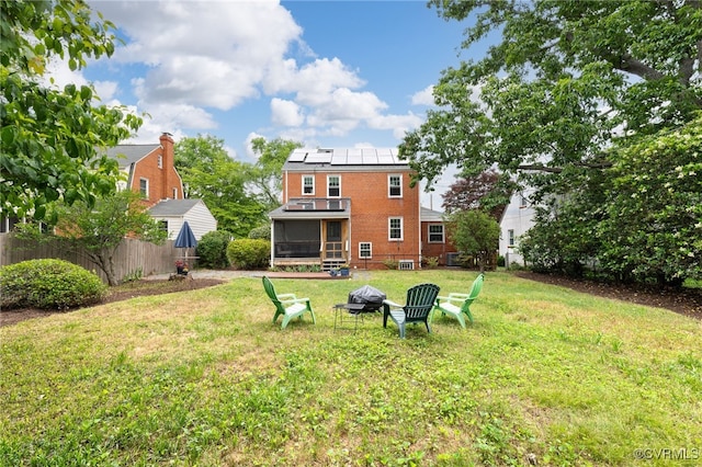 back of property featuring a sunroom, roof mounted solar panels, a fire pit, and brick siding