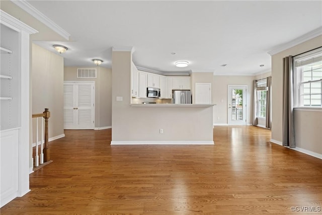 kitchen featuring stainless steel appliances, ornamental molding, white cabinetry, wood finished floors, and a peninsula