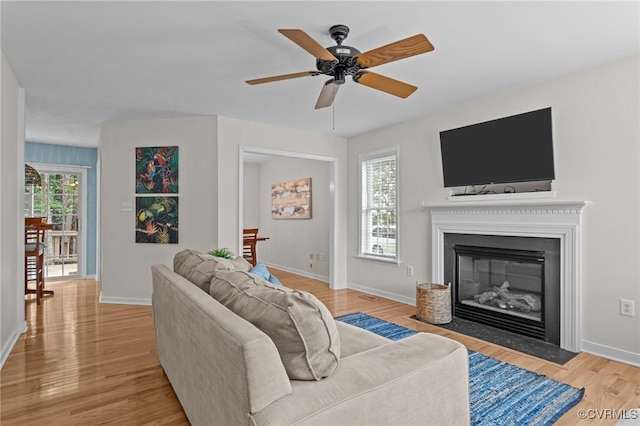 living room featuring light wood finished floors, baseboards, a fireplace with flush hearth, and ceiling fan