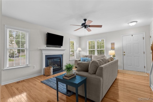 living room with light wood-style flooring, plenty of natural light, a ceiling fan, and baseboards