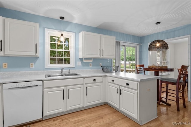 kitchen featuring white dishwasher, a sink, a peninsula, and light wood-style floors
