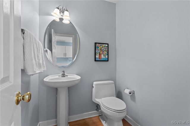 bathroom featuring toilet, wood finished floors, baseboards, and a sink