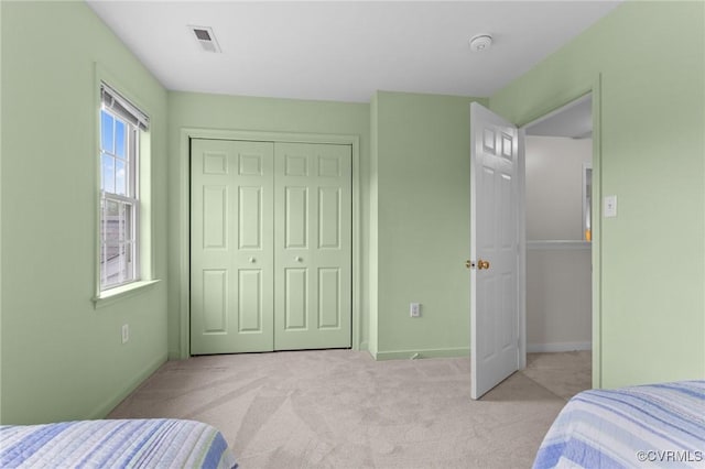 bedroom featuring light colored carpet, baseboards, and a closet