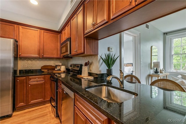 601 Roseneath Rd Unit U11, Richmond, VA 23221 - kitchen featuring stainless steel appliances, a sink, light wood-style floors, brown cabinetry, and dark stone counters