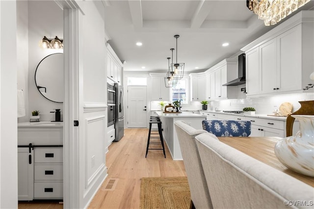 kitchen featuring wall chimney exhaust hood, recessed lighting, a kitchen breakfast bar, light wood-style floors, and white cabinets