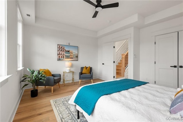 bedroom featuring baseboards, light wood-type flooring, a raised ceiling, and a ceiling fan