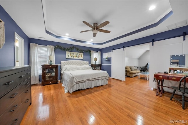 bedroom featuring a barn door, a raised ceiling, light wood-style floors, multiple windows, and crown molding