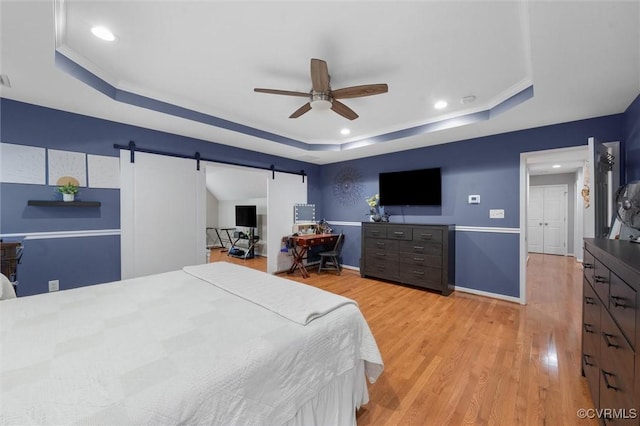bedroom featuring a raised ceiling, a barn door, light wood-style flooring, recessed lighting, and baseboards