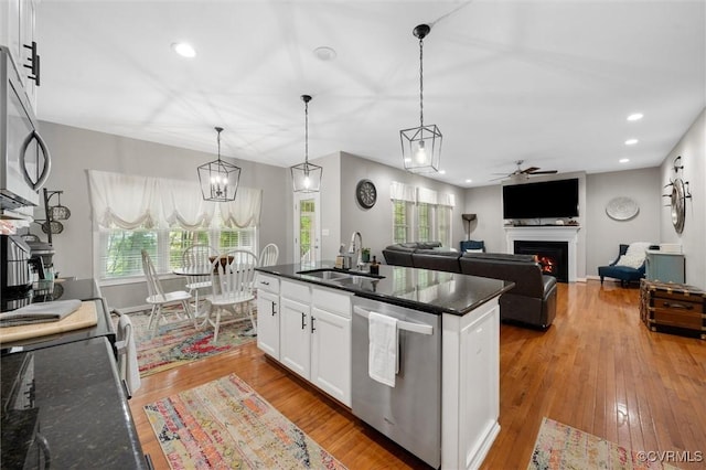 kitchen featuring a sink, stainless steel appliances, ceiling fan, a warm lit fireplace, and white cabinetry