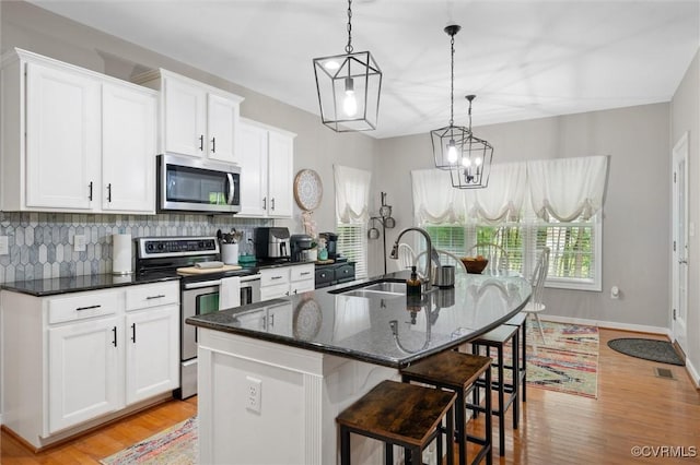 kitchen featuring appliances with stainless steel finishes, a sink, tasteful backsplash, a center island with sink, and light wood-style floors