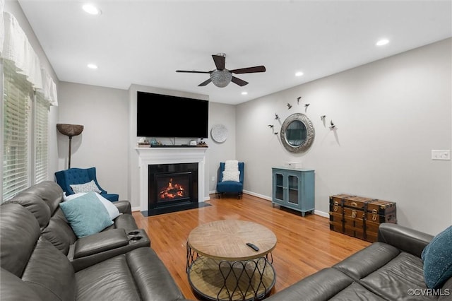 living area featuring a ceiling fan, a fireplace with flush hearth, recessed lighting, wood finished floors, and baseboards