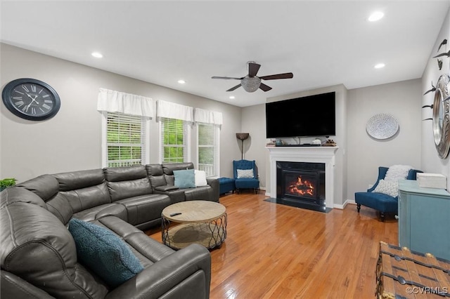 living area featuring a ceiling fan, a fireplace with flush hearth, recessed lighting, light wood-style floors, and baseboards