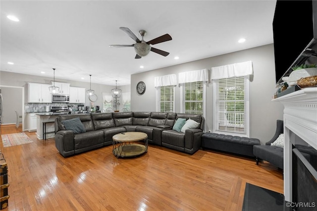 living room featuring ceiling fan, light wood-style flooring, recessed lighting, and a fireplace with flush hearth