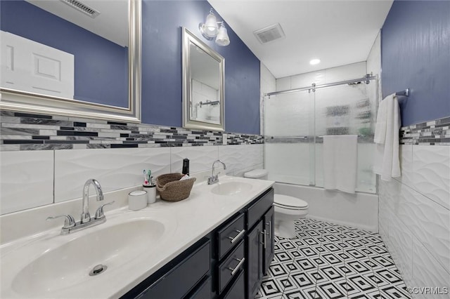 bathroom featuring tile walls, toilet, double vanity, and combined bath / shower with glass door