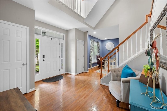 foyer entrance featuring light wood finished floors, stairs, baseboards, a high ceiling, and recessed lighting