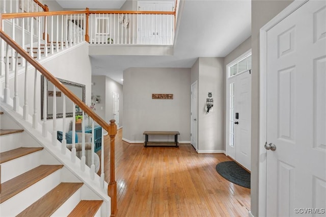 foyer featuring wood-type flooring, baseboards, stairway, and a towering ceiling