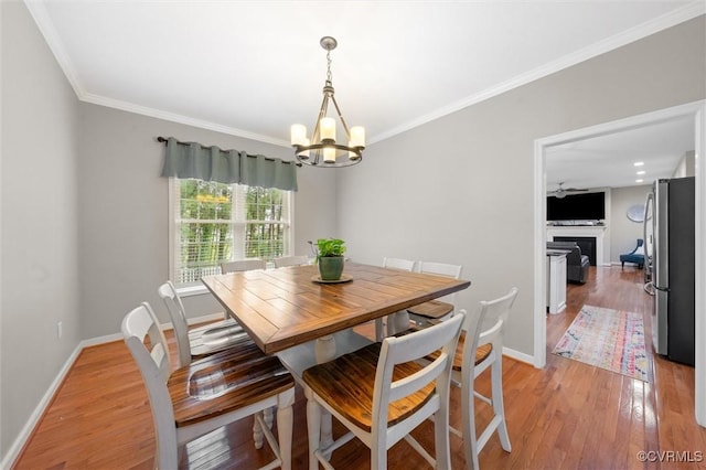 dining room with a chandelier, crown molding, baseboards, light wood-style floors, and a fireplace