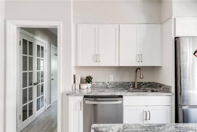 kitchen with appliances with stainless steel finishes, a sink, light stone countertops, white cabinets, and light wood-type flooring