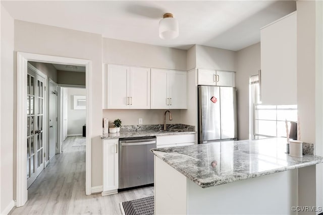 kitchen with stainless steel appliances, white cabinetry, light wood-style floors, and light stone counters
