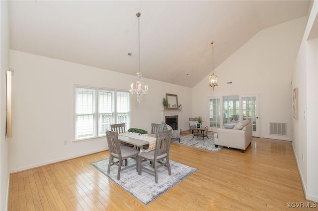 dining space with a fireplace, light wood-style flooring, high vaulted ceiling, a chandelier, and baseboards