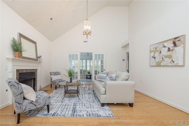 living area featuring high vaulted ceiling, a premium fireplace, light wood-type flooring, and baseboards