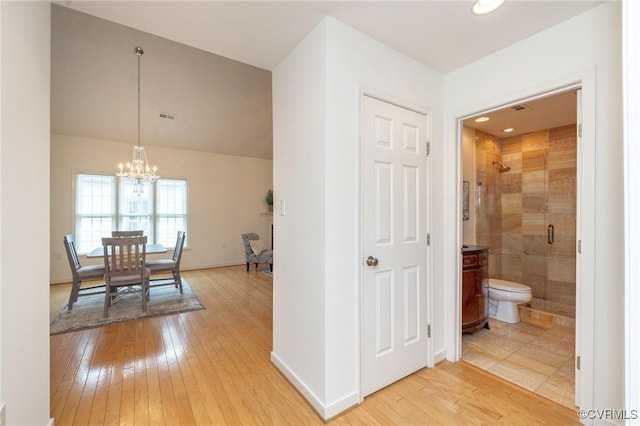hallway featuring light wood-style flooring, a chandelier, and baseboards