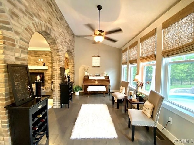 living area featuring wood finished floors, vaulted ceiling, baseboards, ceiling fan, and brick wall