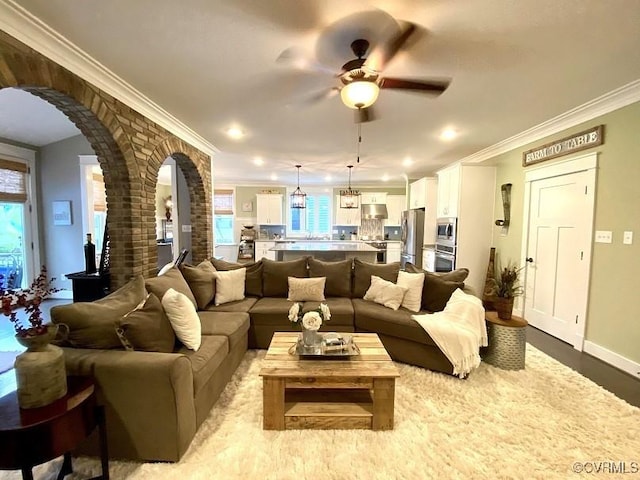 living room with arched walkways, a ceiling fan, crown molding, baseboards, and wood finished floors