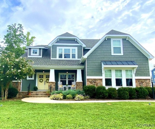 craftsman house featuring stone siding, a front lawn, covered porch, and a shingled roof