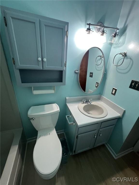 full bath with wood finished floors, vanity, toilet, baseboards, and a tub to relax in
