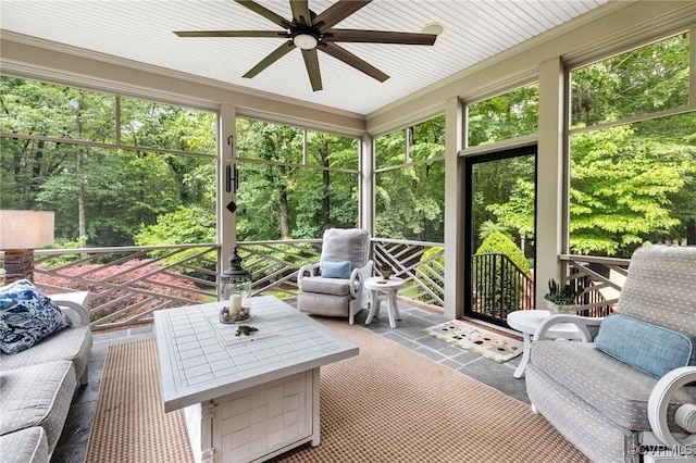 sunroom / solarium with a ceiling fan and view of wooded area