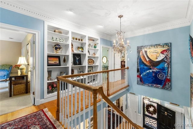 corridor with an upstairs landing, a chandelier, wood finished floors, and ornamental molding