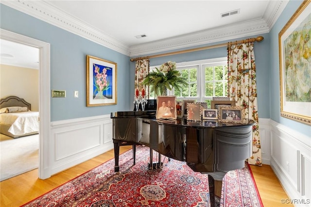 living area with wood finished floors, ornamental molding, wainscoting, and a decorative wall