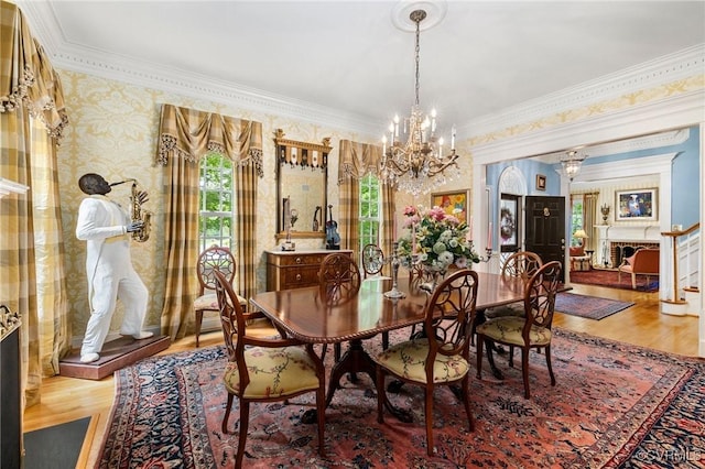 dining room featuring a chandelier, plenty of natural light, wood finished floors, ornamental molding, and wallpapered walls