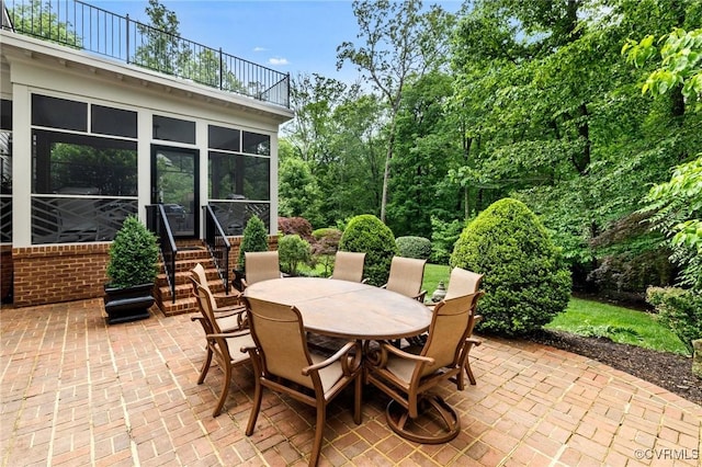 view of patio / terrace featuring a balcony, outdoor dining area, and a sunroom
