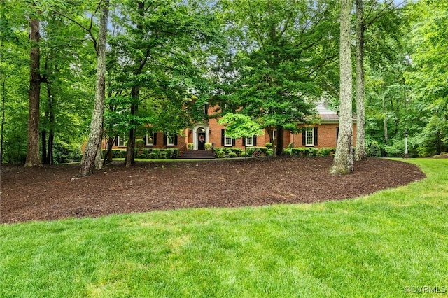 view of property hidden behind natural elements with a front yard and brick siding