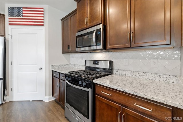 kitchen featuring stainless steel appliances, dark wood-style flooring, tasteful backsplash, and light stone countertops