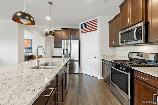 kitchen with appliances with stainless steel finishes, a sink, dark wood finished floors, light stone countertops, and decorative backsplash