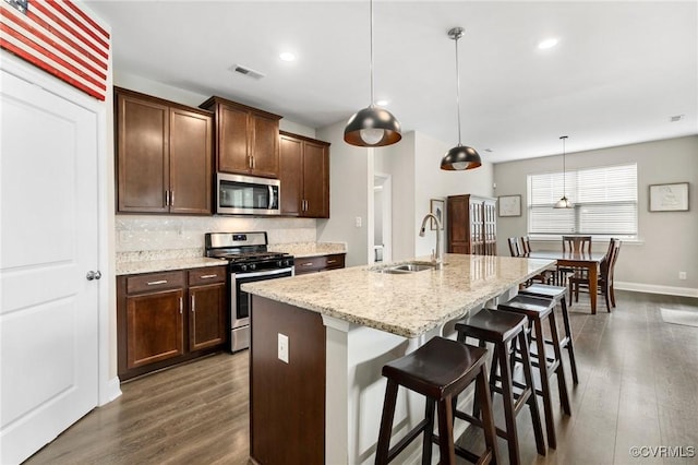 kitchen featuring appliances with stainless steel finishes, a sink, backsplash, dark wood-type flooring, and an island with sink