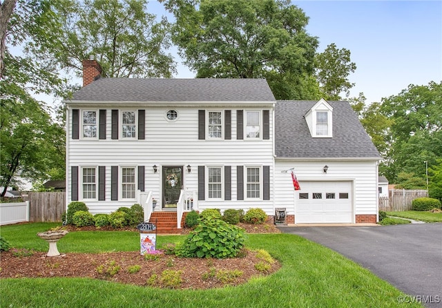 colonial home with an attached garage, a chimney, asphalt driveway, and a shingled roof