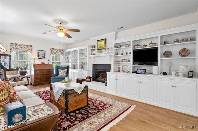 living area with ceiling fan, light wood-type flooring, and a fireplace