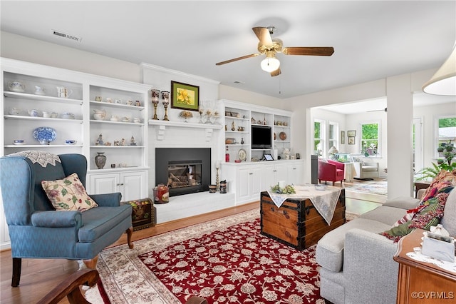 living area featuring ceiling fan, a large fireplace, and wood finished floors