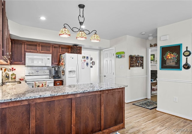 kitchen with white appliances, a sink, light stone counters, light wood-style flooring, and recessed lighting