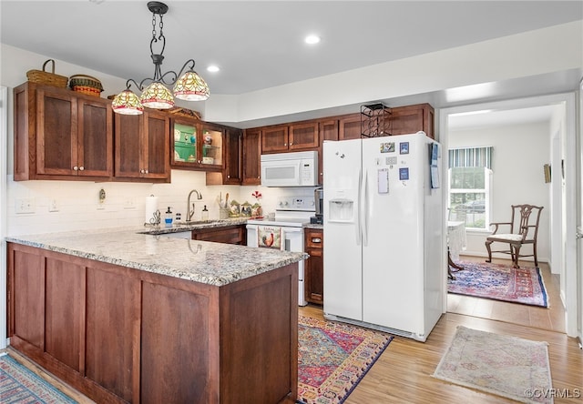 kitchen with white appliances, a peninsula, light stone counters, glass insert cabinets, and a sink