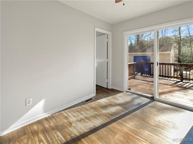 spare room featuring baseboards, wood finished floors, a fireplace, and a ceiling fan